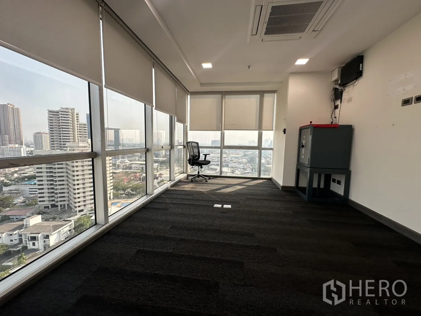 Office Space for rent - Carpeted office room with panoramic windows, blinds and an equipment cabinet.
