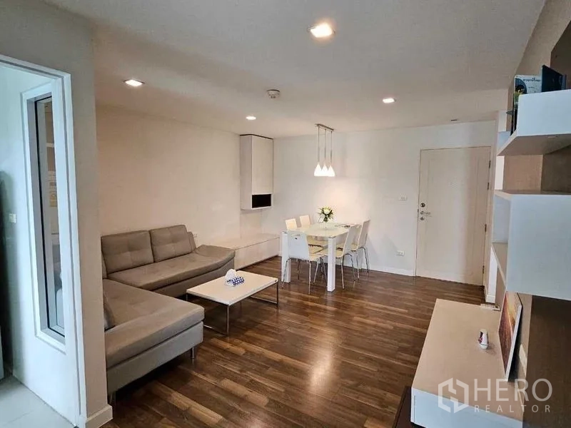 Condominium for sale in Watthana, Bangkok - Bright living and dining area with L-shaped sofa, wood floors, and pendant lights in a modern condo.