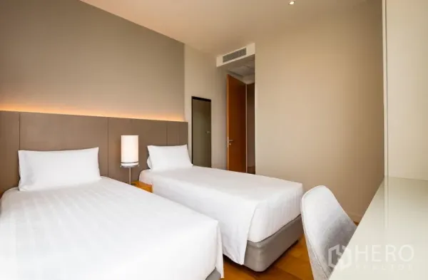 Condominium for rent in Bang Kho Laem, Bangkok - Twin bedroom with soft lighting, bedside lamp and built‑in desk on hardwood flooring.