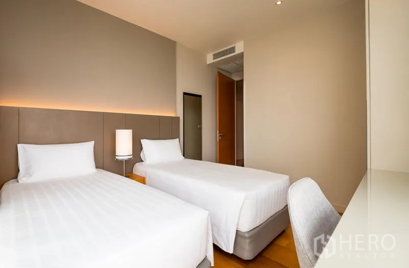 Condominium for rent in Bang Kho Laem, Bangkok - Twin bedroom with soft lighting, bedside lamp and built‑in desk on hardwood flooring.