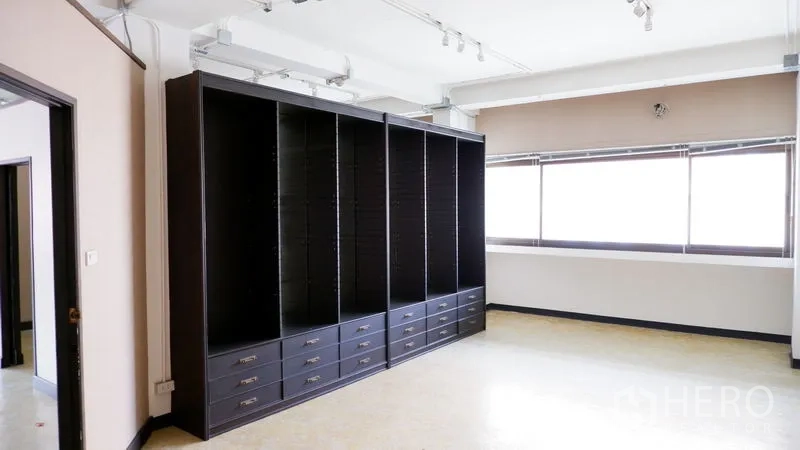 办公空间 出租在Watthana, Bangkok - 采光充足的工作区，整面深色内置柜与抽屉，旁有宽大窗户。