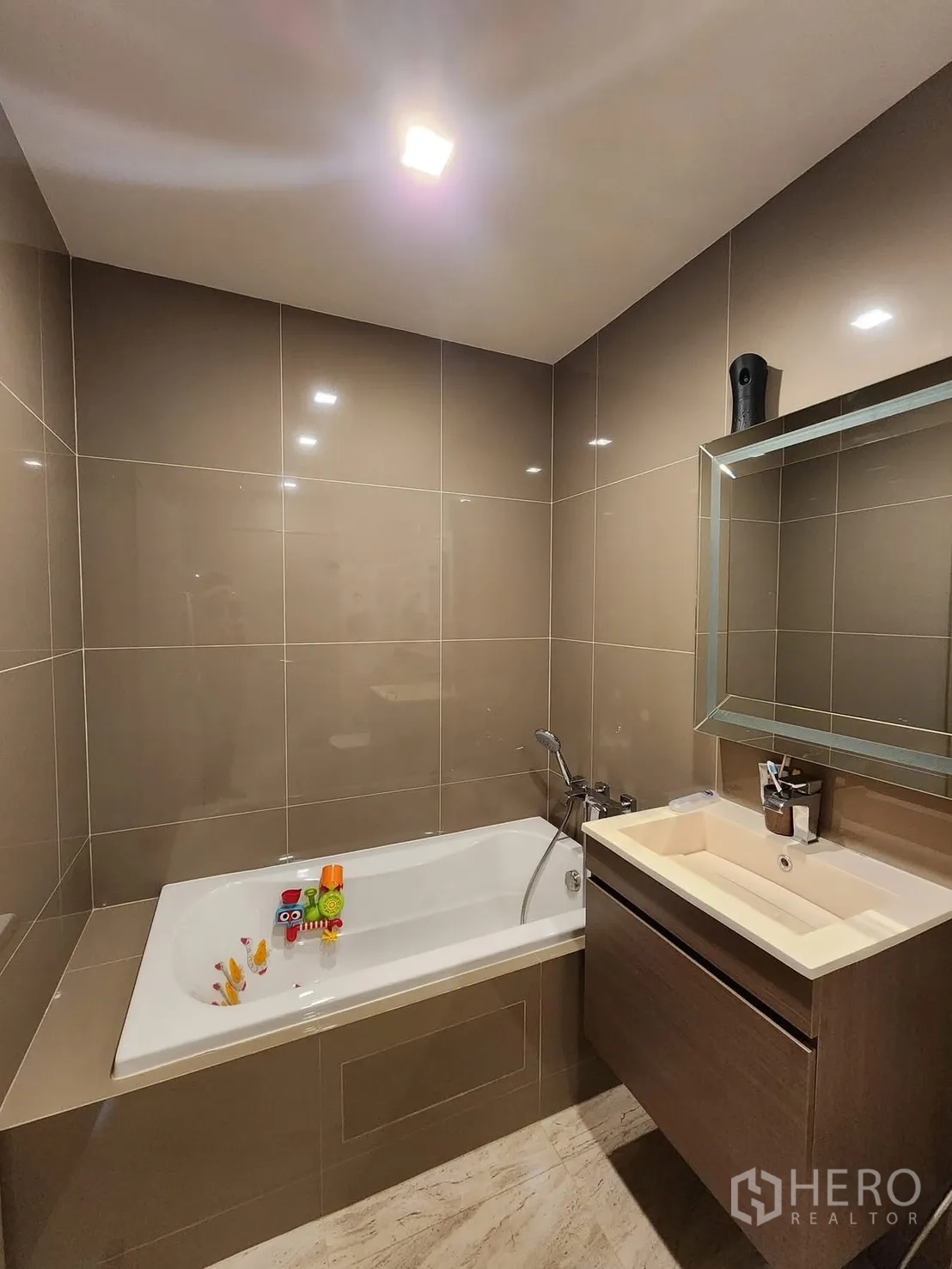 公寓 for rent in Watthana, Bangkok - 浴室配嵌入式浴缸、盥洗柜与镜柜，暖色系瓷砖。