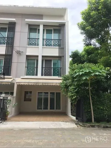 Townhouse for rent or sale in Suan Luang, Bangkok - Three-storey Suan Luang townhouse exterior with covered carport, balconies, and mature trees at the side.