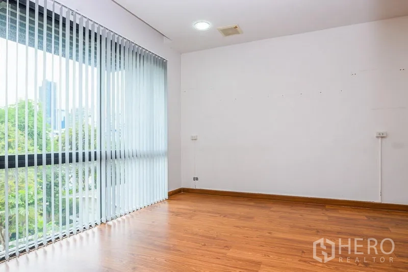 Townhouse for rent in Watthana, Bangkok - Corner room with vertical blinds and full-height windows showing city and tree views.