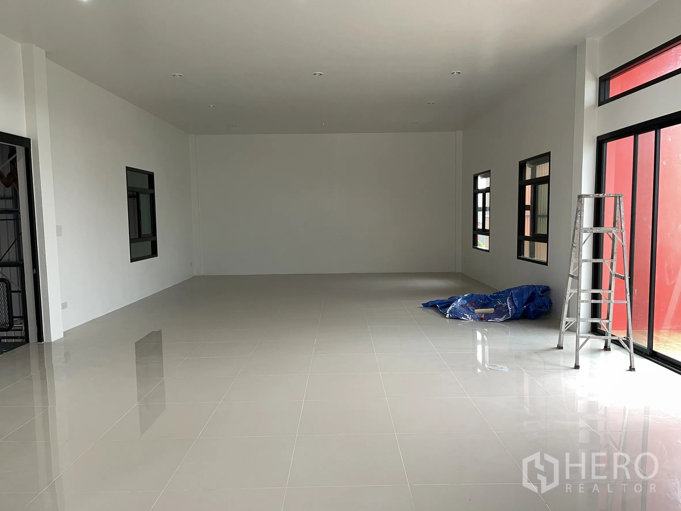Factory for rent or sale in Lam Luk Ka, Pathum Thani - Wide office floor with large windows, sliding glass entry, and a ladder on the side.