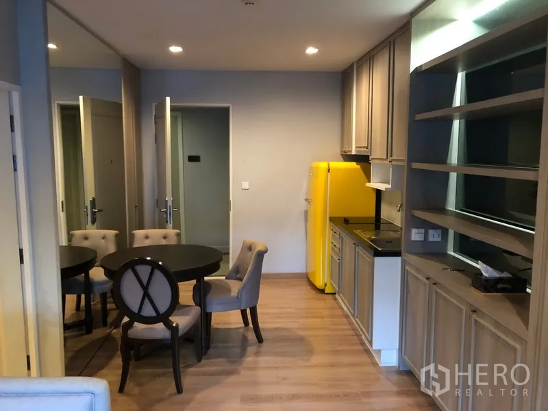 Condominium for rent in Pathum Wan, Bangkok - Open kitchen and dining area with round table, upholstered chairs, yellow fridge, and built-in storage.