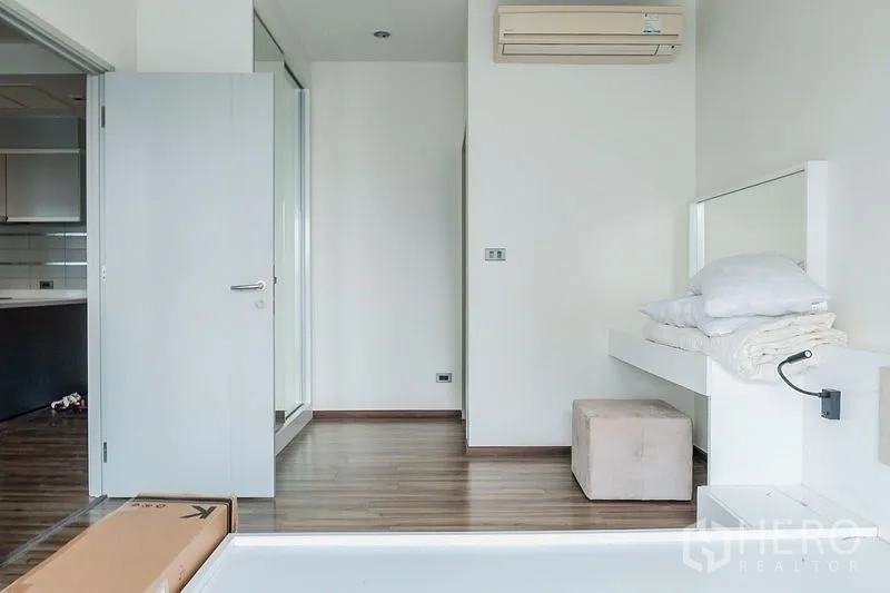Condominium for rent in Khlong Toei, Bangkok - Minimalist bedroom entrance with white walls, wood floors and a wall-mounted air conditioner.