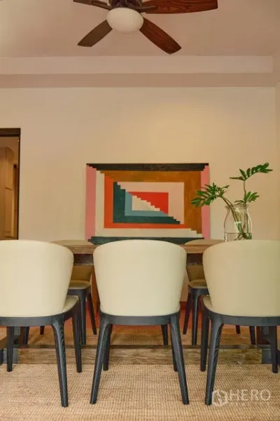 Detached House for rent in Watthana, Bangkok - Dining area with upholstered chairs and colorful geometric wall art under a ceiling fan.