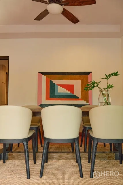 Detached House for rent in Watthana, Bangkok - Dining area with upholstered chairs and colorful geometric wall art under a ceiling fan.