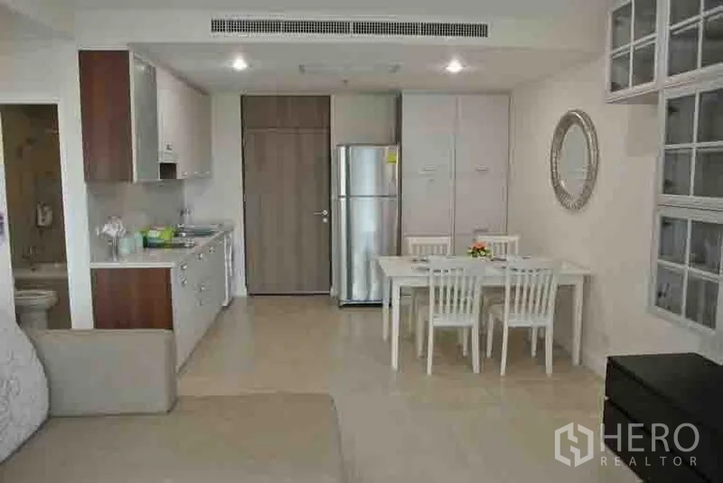 Condominium for rent in Khlong Toei, Bangkok - Open-plan dining area and kitchen with white cabinetry, refrigerator and four-seat table.