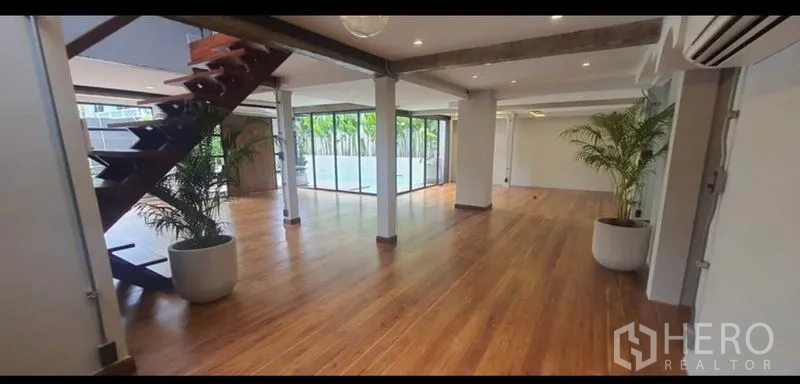 带办公室的家 出租或出售在Khlong Toei, Bangkok - 宽敞开放式室内，木地板、外露梁、楼梯与落地窗，面向绿植。