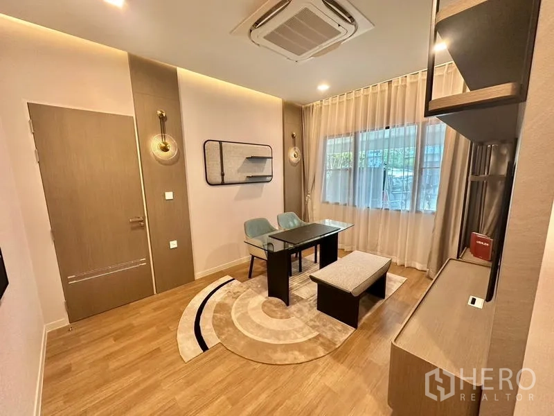 Detached House for rent in Samut Prakan - Cozy study room with glass desk, accent lighting, wood floors and a large curtained window.