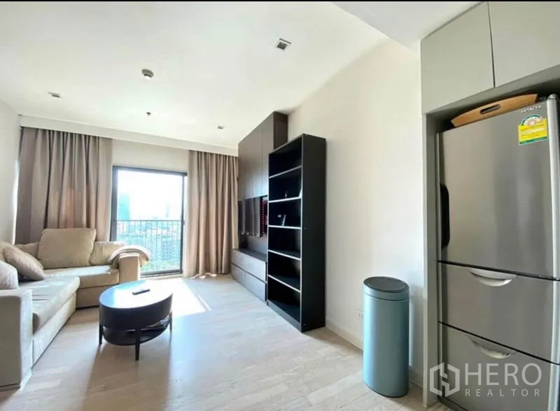 Condominium for rent in Khlong Toei, Bangkok - Living room with beige sofas, built-in TV wall and shelving, and a window to the balcony.