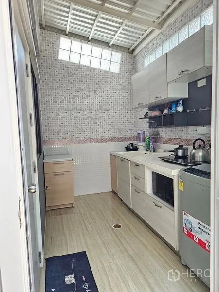 Townhouse for rent - Compact Thai kitchen with mosaic tiles, cabinetry, sink and electric cooktop.