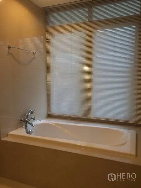 Condominium for rent in Watthana, Bangkok - Bathtub alcove with wall-mounted faucet and frosted blinds in a neutral-toned bathroom.