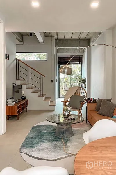 Townhouse for rent in Huai Khwang, Bangkok - Open living area with TV console and staircase beside floor-to-ceiling windows to the patio.