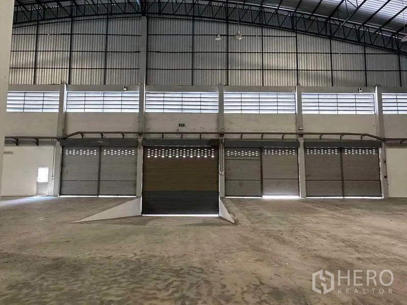 Warehouse for rent in Samut Prakan - Row of roller shutter doors with a central drive-in ramp for loading and unloading.