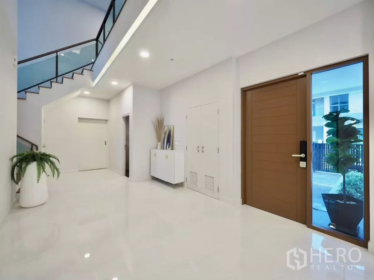 独立式住宅 出租在Bang Phli, Samut Prakan - 宽敞玄关，木门、亮面地砖与玻璃楼梯栏杆。