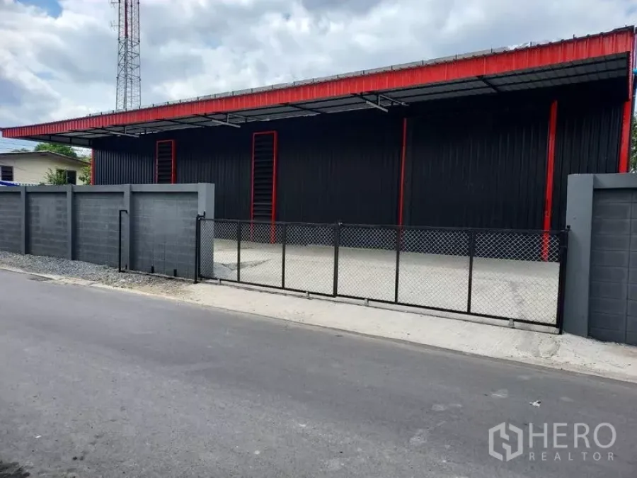 Warehouse for rent in Bang Kapi, Bangkok - Street view of a gated black-and-red warehouse with a covered loading apron and secure perimeter wall.