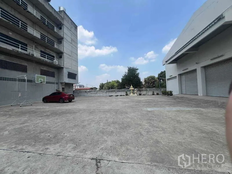 货栈 出租在Lam Luk Ka, Pathum Thani - 仓库前大型混凝土院子，带多扇卷闸装卸口和停车位