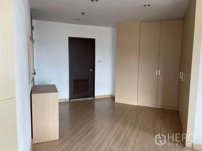 Condominium for rent in Khlong Toei, Bangkok - Room with wood floors, built-in wardrobe and dark wooden door.