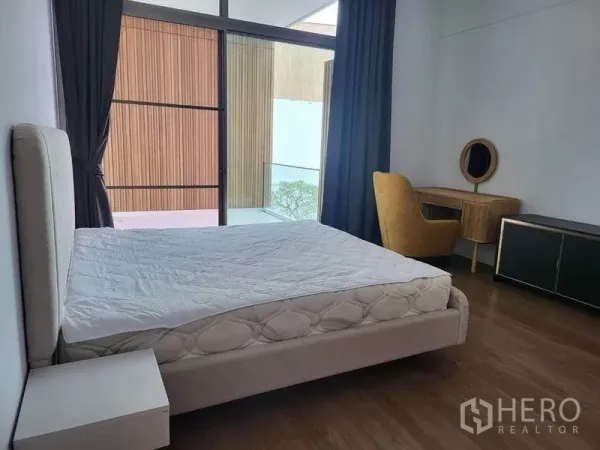 Detached House for rent in Saphan Sung, Bangkok - Modern bedroom with sliding glass door to a balcony, vanity desk and dark drapes overlooking a wood‑panel facade.