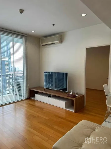 Condominium for rent in Ratchathewi, Bangkok - Living room with TV console, air conditioner, and access to the balcony.