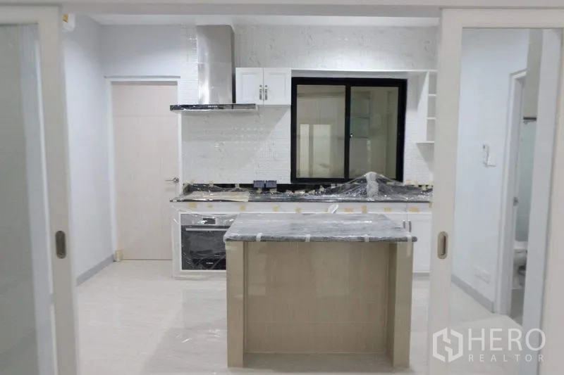 Detached House for sale in Bang Phli, Samut Prakan - Bright modern kitchen with island, built-in oven and range hood behind sliding doors.