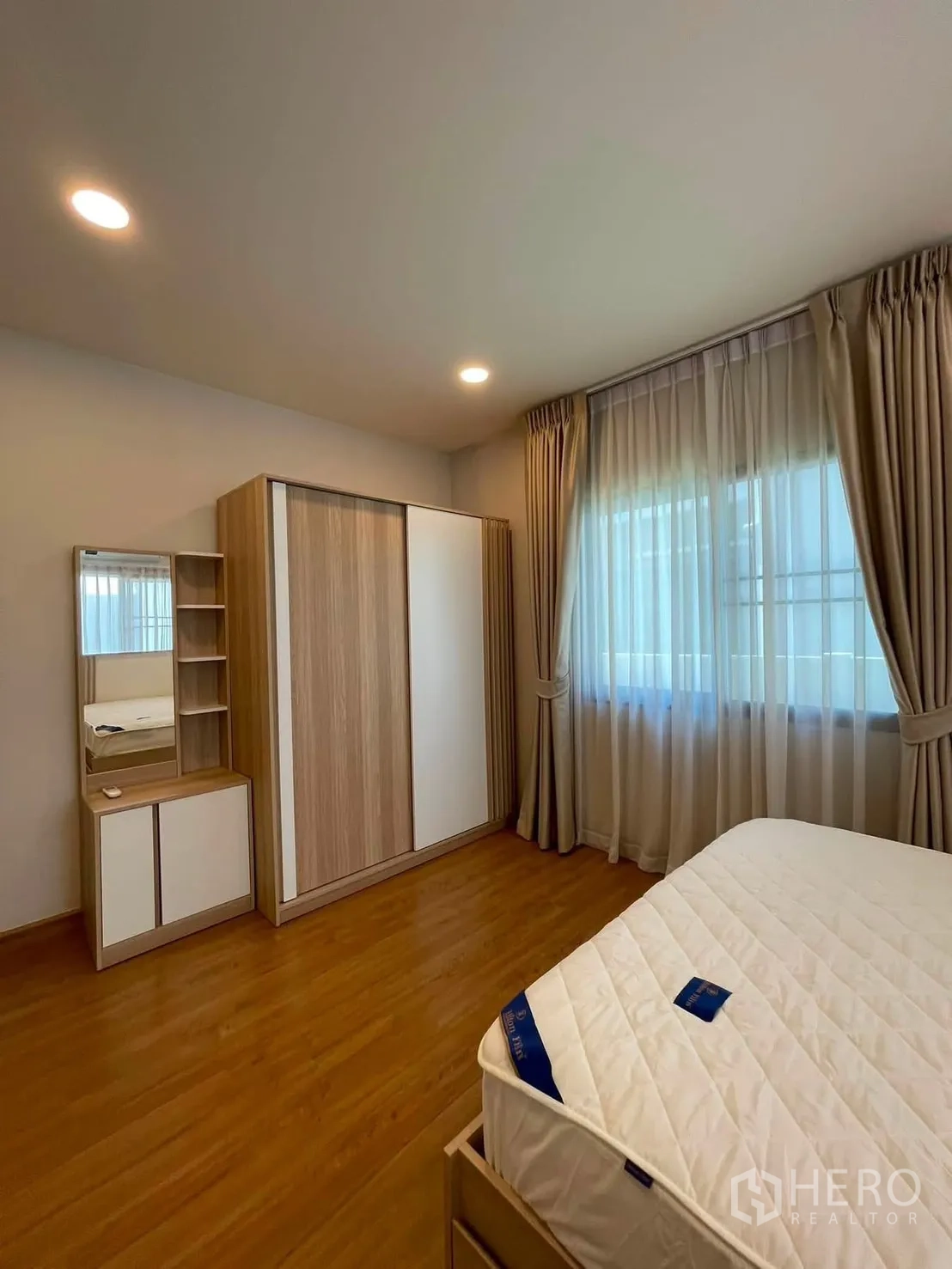 Detached House for rent in Bang Phli, Samut Prakan - Bright bedroom with wood flooring, large wardrobe, dressing table with mirror, and a curtained window.