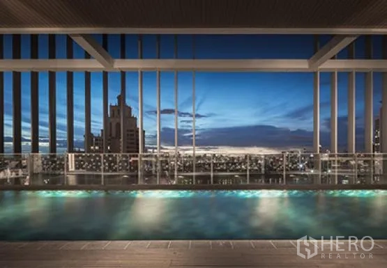 Condominium for rent or sale in Khlong Toei, Bangkok - Rooftop swimming pool at dusk overlooking the Bangkok skyline with seating deck.