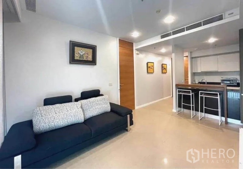 Condominium for rent in Khlong San, Bangkok - Open‑plan living room with dark sofa and a breakfast bar adjoining the kitchen.
