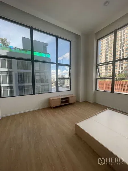 Condominium for rent in Khlong Toei, Bangkok - Bright living area with floor-to-ceiling corner windows and wood floors overlooking city buildings.