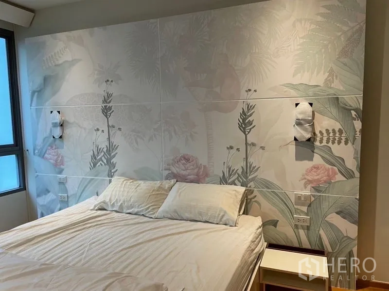 Condominium for sale in Khlong Toei, Bangkok - Master bedroom with floral feature wall and king bed near a window.