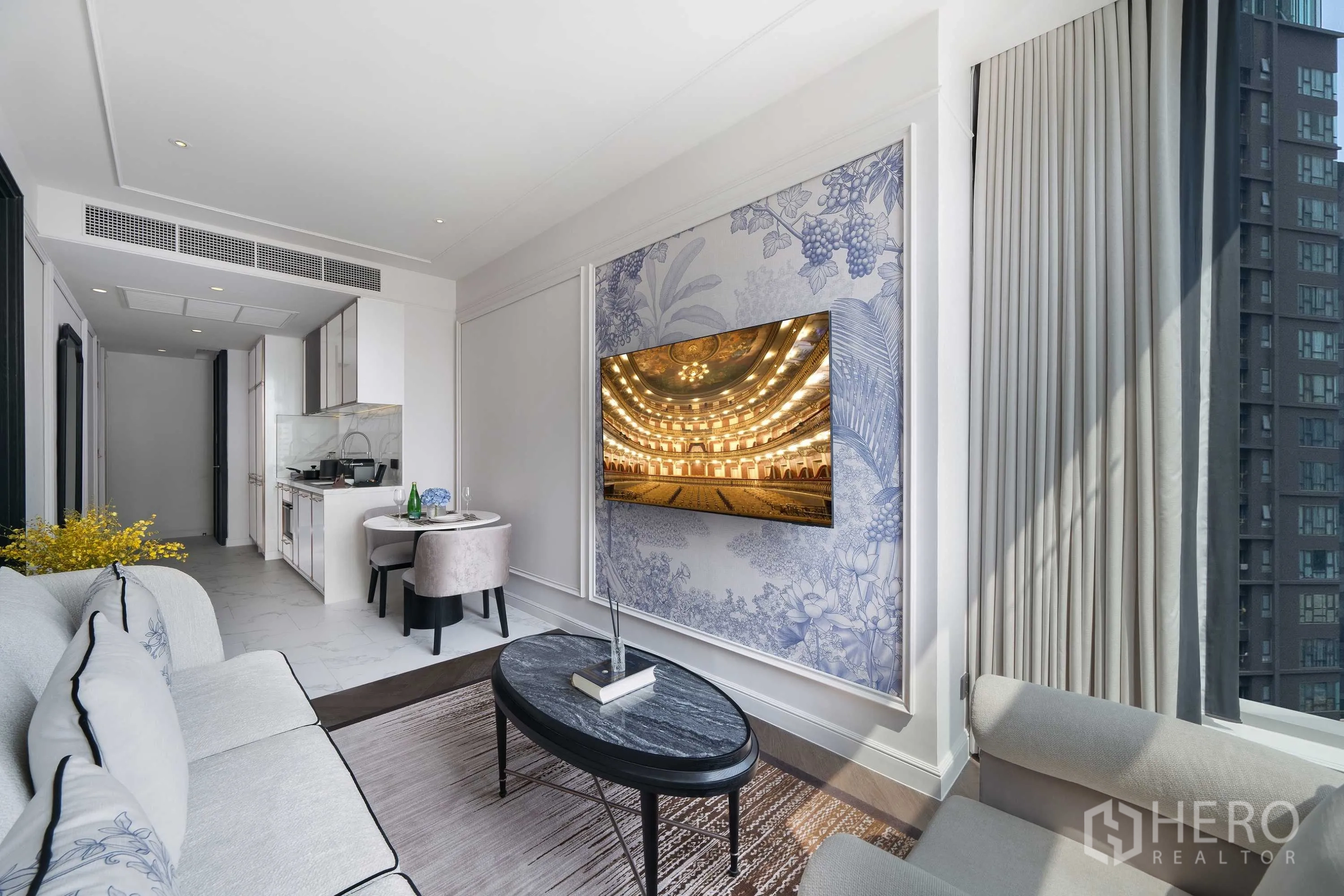 คอนโด for rent in Khlong Toei, Bangkok - มุมนั่งเล่นมีทีวีติดผนังลายตกแต่ง โต๊ะกาแฟทรงรี ผ้าม่านสูง และวิวตึกเมืองภายนอก