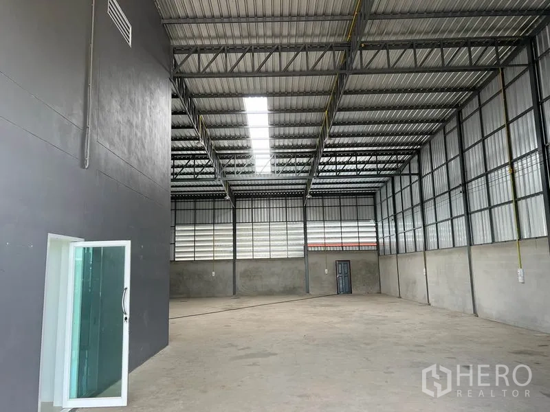 Warehouse for rent in Lam Luk Ka, Pathum Thani - Spacious high-ceiling warehouse hall with steel trusses and skylight panels.