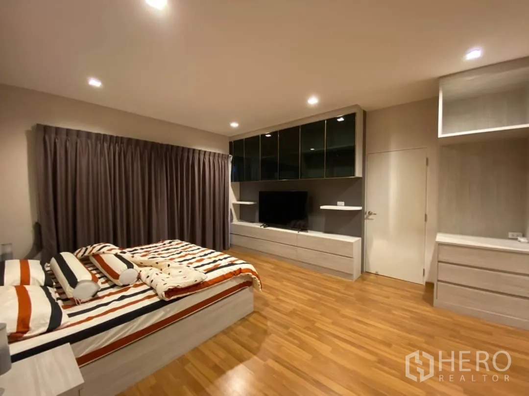 Detached House for rent or sale in Prawet, Bangkok - Master bedroom angle showing wood floors and built-in TV cabinet with storage.