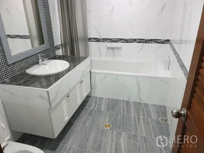 Condominium for rent in Watthana, Bangkok - Modern bathroom with marble-style tiles, a vanity sink, and a bathtub with shower curtain.