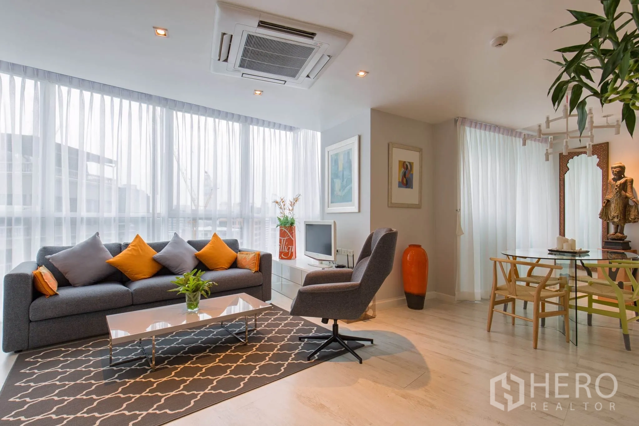 คอนโด ให้เช่าในPathum Wan, Bangkok - ห้องนั่งเล่นและรับประทานอาหารแบบเปิดโล่ง โปร่งสว่างด้วยผนังกระจก โซฟาสีเทาหมอนสีส้ม เก้าอี้เดี่ยว และพื้นไม้โทนอ่อน