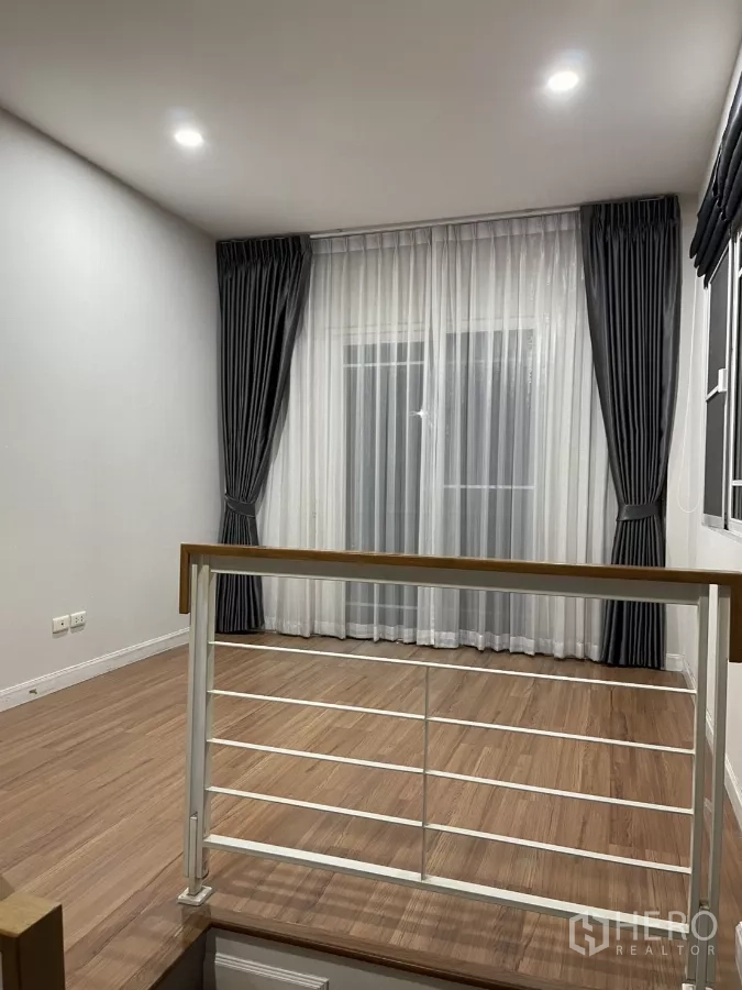 Detached House for rent in Bang Kapi, Bangkok - Upstairs family area with wood flooring and sheer curtains over a balcony door.