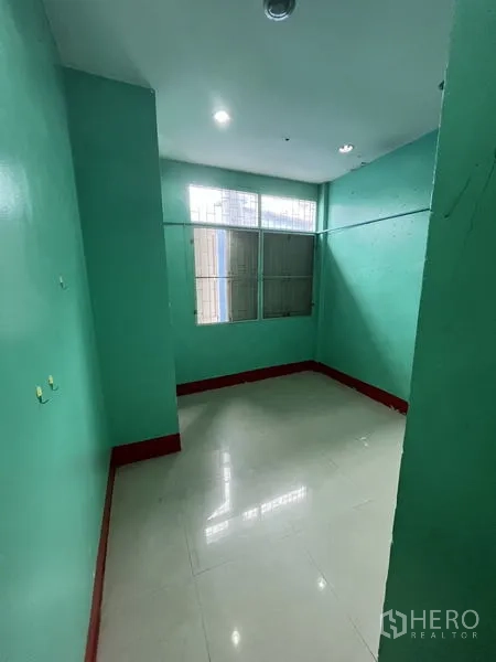 Shophouse for rent in Khlong Toei, Bangkok - Compact room painted green with a window and shiny floor tiles.