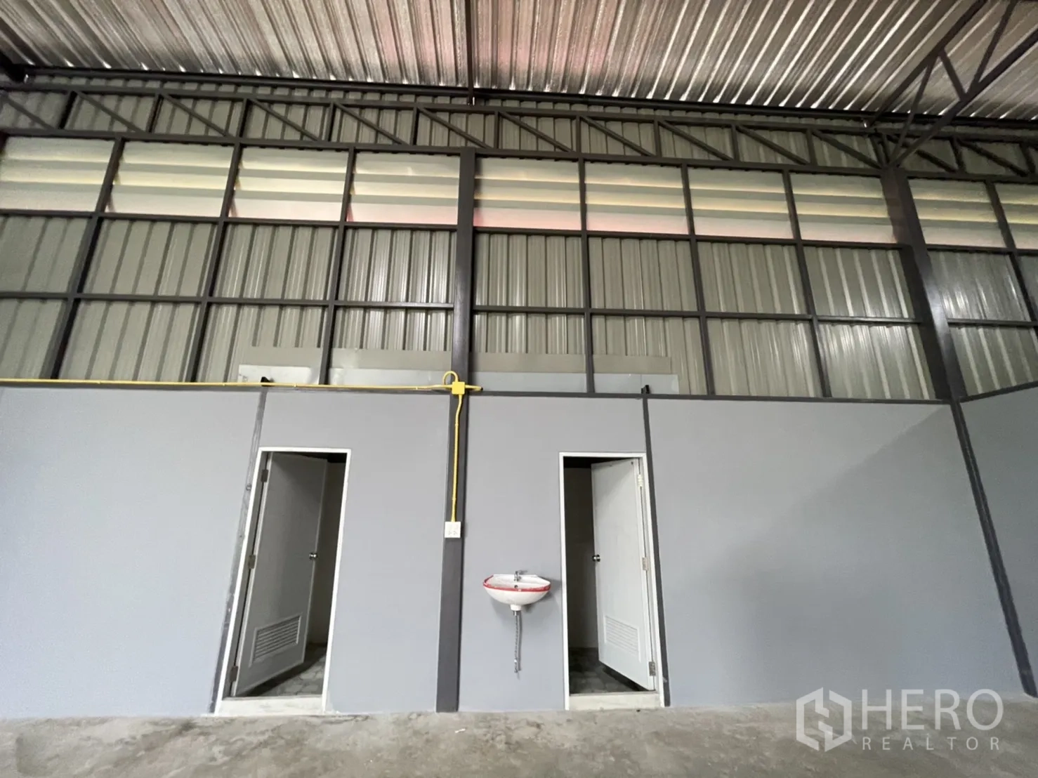 Factory for rent in Khlong Luang, Pathum Thani - Pair of restrooms with white doors and a wall-mounted basin inside the factory.