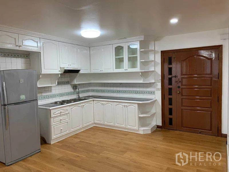 Condominium for rent or sale in Watthana, Bangkok - Bright U-shaped kitchen with white cabinetry, tiled backsplash, cooktop, and a stainless refrigerator.