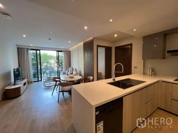 Condominium for rent in Watthana, Bangkok - Open-plan kitchen and living space leading to a leafy balcony, filled with natural light.