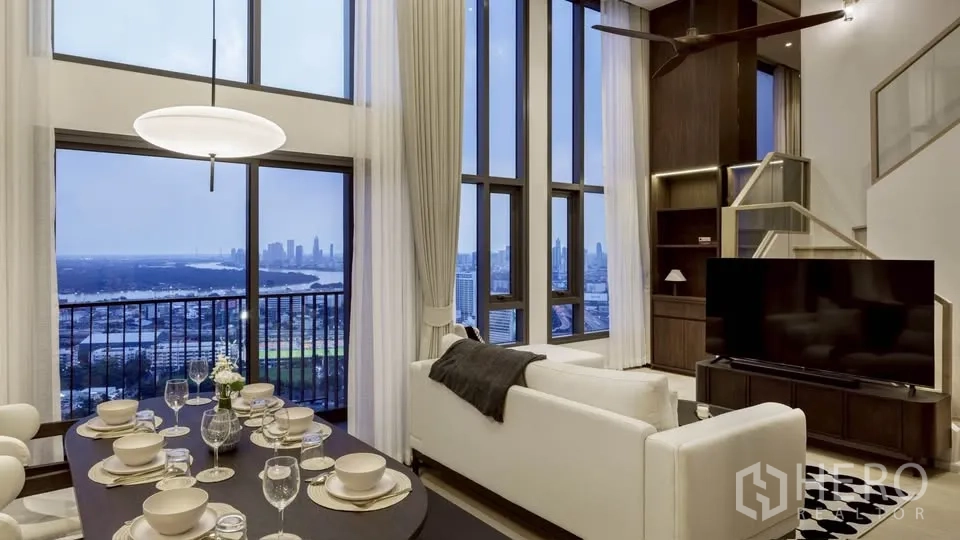 Condominium for rent in Khlong Toei, Bangkok - Double-height living and dining with floor-to-ceiling windows, city and river views, white sofa, TV, and staircase.