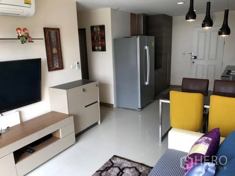 Condominium for rent in Khlong Toei, Bangkok - Bright living room with wall-mounted TV, console, dining set, and stainless steel refrigerator.