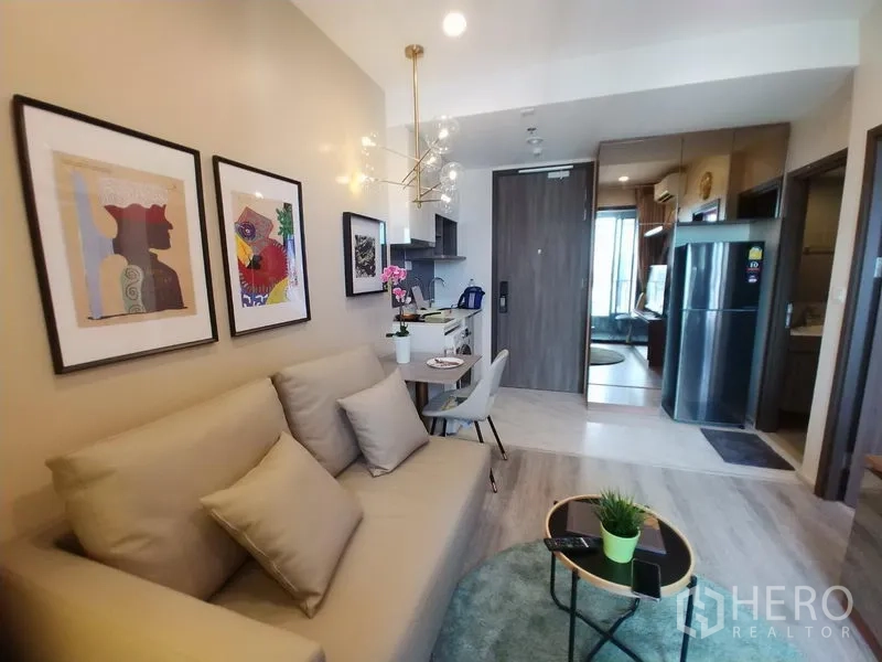 公寓 出租在Huai Khwang, Bangkok - 开放式起居区，沙发与圆形地毯，紧凑厨房与镜面收纳柜。
