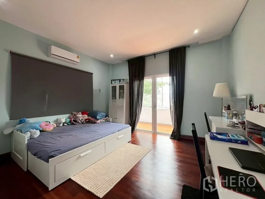 Detached House for rent in Phra Khanong, Bangkok - Spacious bedroom with study desk and doors to a balcony.