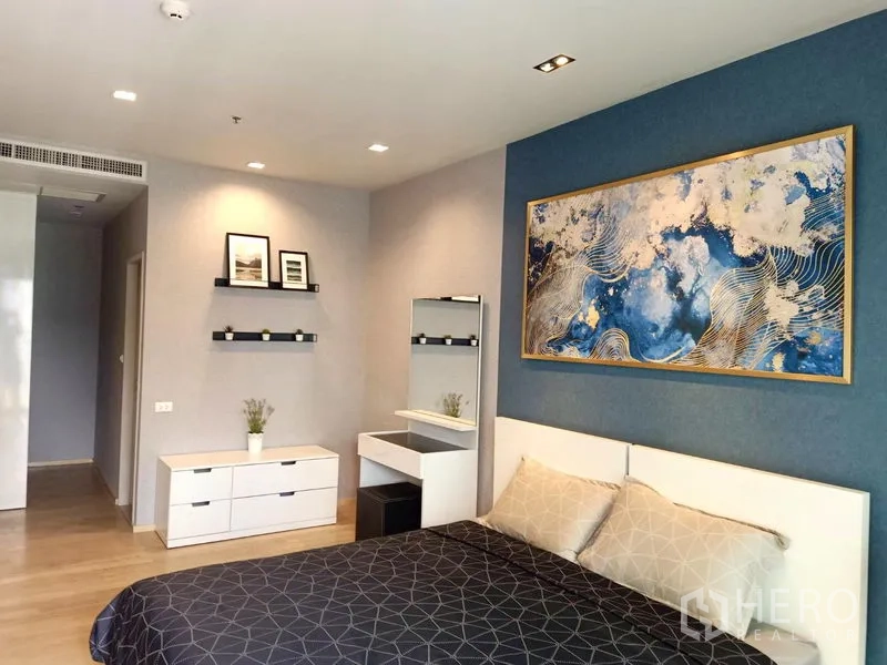 Condominium for rent in Bangkok - Serene bedroom with blue accent wall, white bed, dresser and vanity.