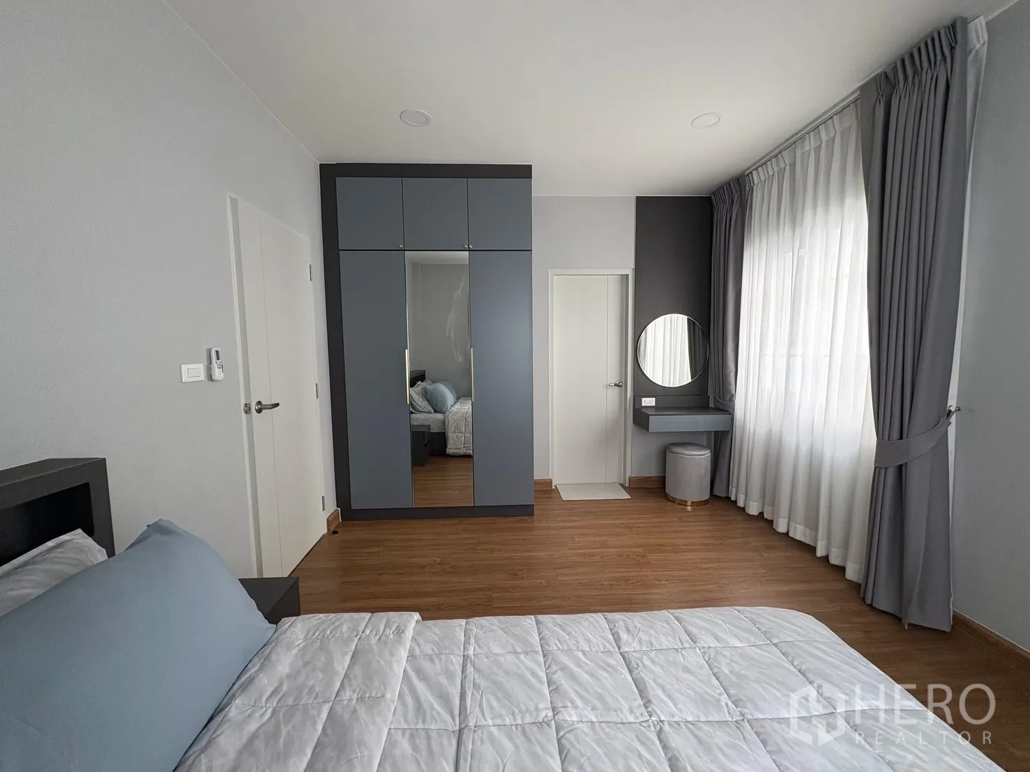 บ้าน for rent in Bang Phli, Samut Prakan - ห้องนอนหลักพร้อมตู้เสื้อผ้าบิลท์อินบานกระจก โต๊ะเครื่องแป้ง และผ้าม่านบานใหญ่ พื้นไม้.