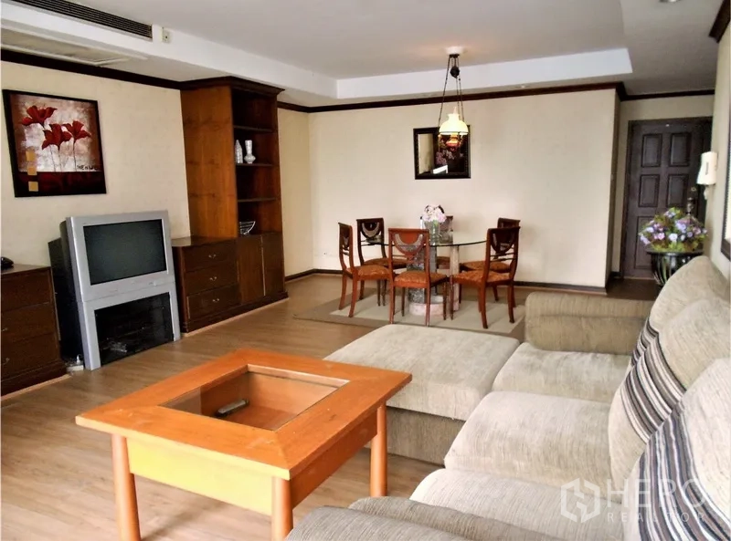 Condominium for rent or sale in Watthana, Bangkok - Open-plan living room with sectional sofa, TV unit, dining area, and built-in shelving.
